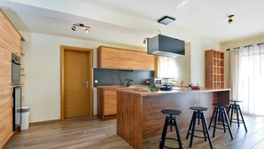 A modern kitchen with wooden cabinets, a central island with stools, and a built-in oven.