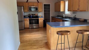 A modern kitchen with wooden cabinets, stainless steel appliances, a blue countertop, and a bar stool area. - Waterfront Home for Summer/Winter Fun (Wakefield)