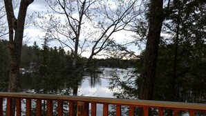 A deck with a fire pit and a chair labeled "RED SOX", overlooking a lake surrounded by trees. - Waterfront Home for Summer/Winter Fun (Wakefield)