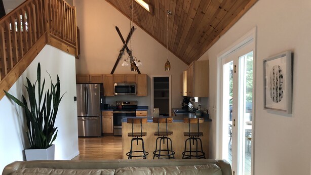 A modern kitchen with wooden cabinets, stainless steel appliances, and a bar area with stools. - Waterfront Home for Summer/Winter Fun (Wakefield)