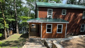 A wooden cabin with a porch and stone steps leading to a door. - Waterfront Home for Summer/Winter Fun (Wakefield)