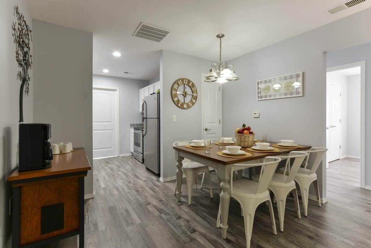 A dining area with a wooden table, white chairs, and a clock on the wall.