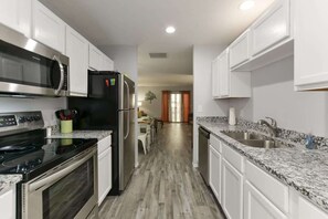 Una cocina moderna con armarios blancos, encimera de granito, electrodomésticos de acero inoxidable y suelo de madera.