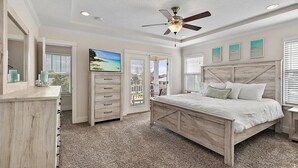 Quarto com cama de madeira, ventilador de teto, televisão e vista para o exterior.