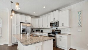 Uma cozinha moderna com armários brancos, bancadas de granito, eletrodomésticos de aço inoxidável e iluminação pendente.