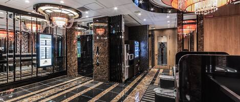 A modern hotel lobby with a marble floor, a central chandelier, and a digital information kiosk.
