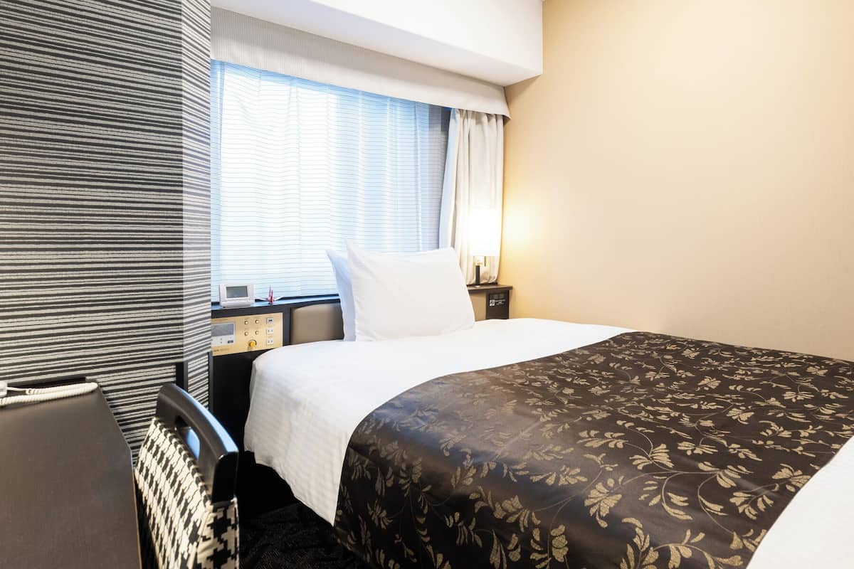 Een hotelkamer met een bed, nachtkastje, lamp en raam met gordijnen.
