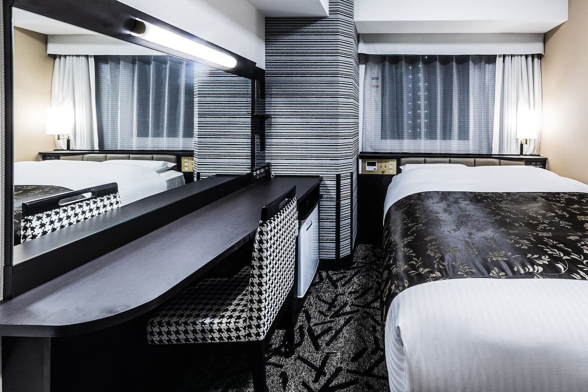 Hotelkamer met een bed, bureau, spiegel, bedieningspaneel en raam met gordijnen.