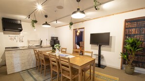 A modern kitchen with a central island, wooden dining table, and chairs. There is a TV mounted on the wall and a potted plant on the floor. - Core Resort House 2 In Ishigaki (Ishigaki)