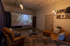A cozy living room with a large screen, leather sofas, and a coffee table. - Core Resort House 2 In Ishigaki (Ishigaki)