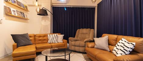 Un salon comprenant un canapé, un fauteuil et une table basse. On y trouve des étagères murales remplies de livres et un projecteur fixé au plafond.