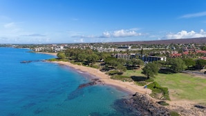 Luftaufnahme einer Küstenlandschaft mit Strand, klarem blauen Wasser und einer Wohngegend mit Gebäuden.