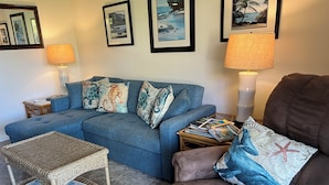 Ein Wohnzimmer mit einem blauen Sofa, einem braunen Sessel, einem Korbtisch mit einer Karte und einem kleinen Beistelltisch mit Zeitschriften.