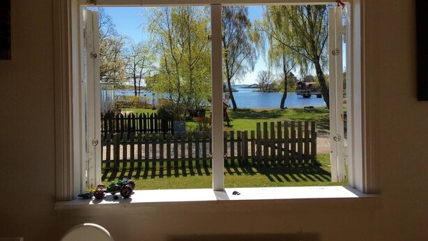 A room with a large window overlooking a lake, a wooden fence, and a small toy car on the windowsill. - Cozy and modern cottage by the beach in the south of Sweden (Djursvik)