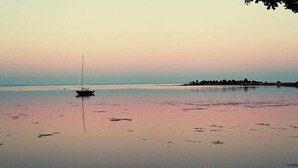 A calm body of water with a sailboat anchored in the center, surrounded by a calm shoreline and a distant tree line. - Cozy and modern cottage by the beach in the south of Sweden (Djursvik)