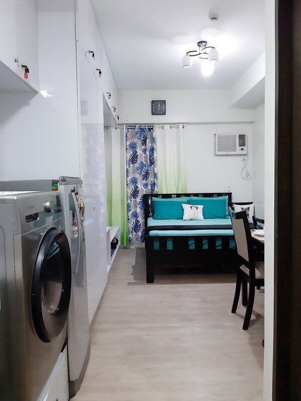 Una habitación pequeña con cama, escritorio y lavadora.