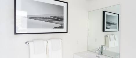 A modern bathroom with a framed photograph, two white towels, a large mirror, and a white sink.