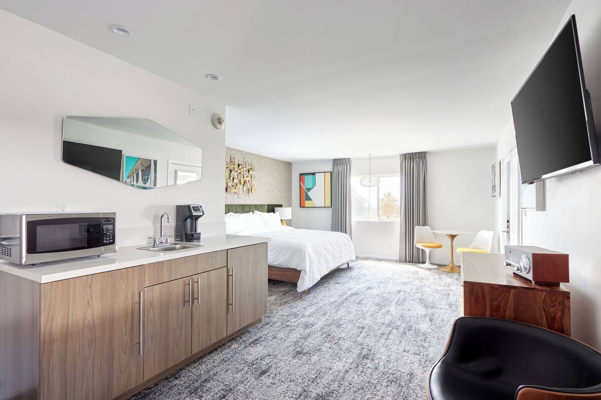 A hotel room with a bed, a desk, a microwave, a coffee maker, a TV, and a large mirror.