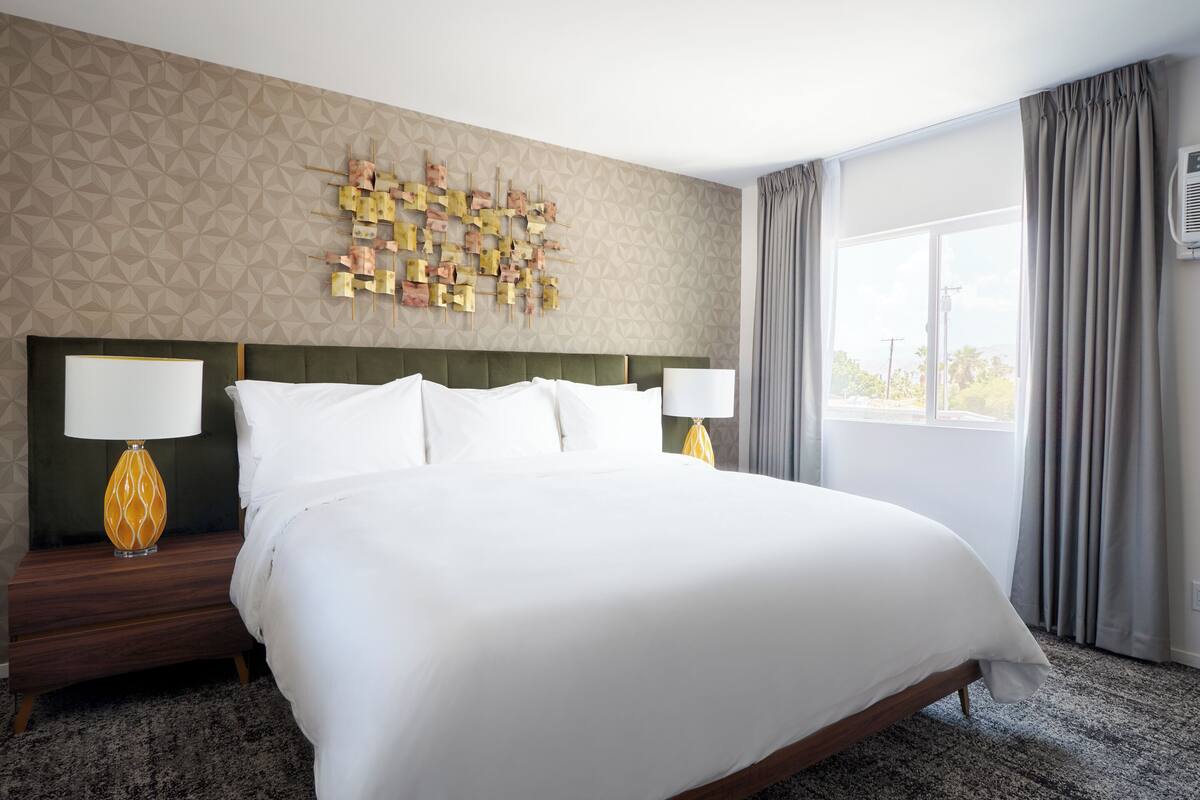A hotel room with a large bed, two bedside tables with lamps, a geometric patterned wall, and a window with curtains.