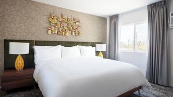 A hotel room with a large bed, two bedside tables with lamps, a geometric patterned wall, and a window with curtains.