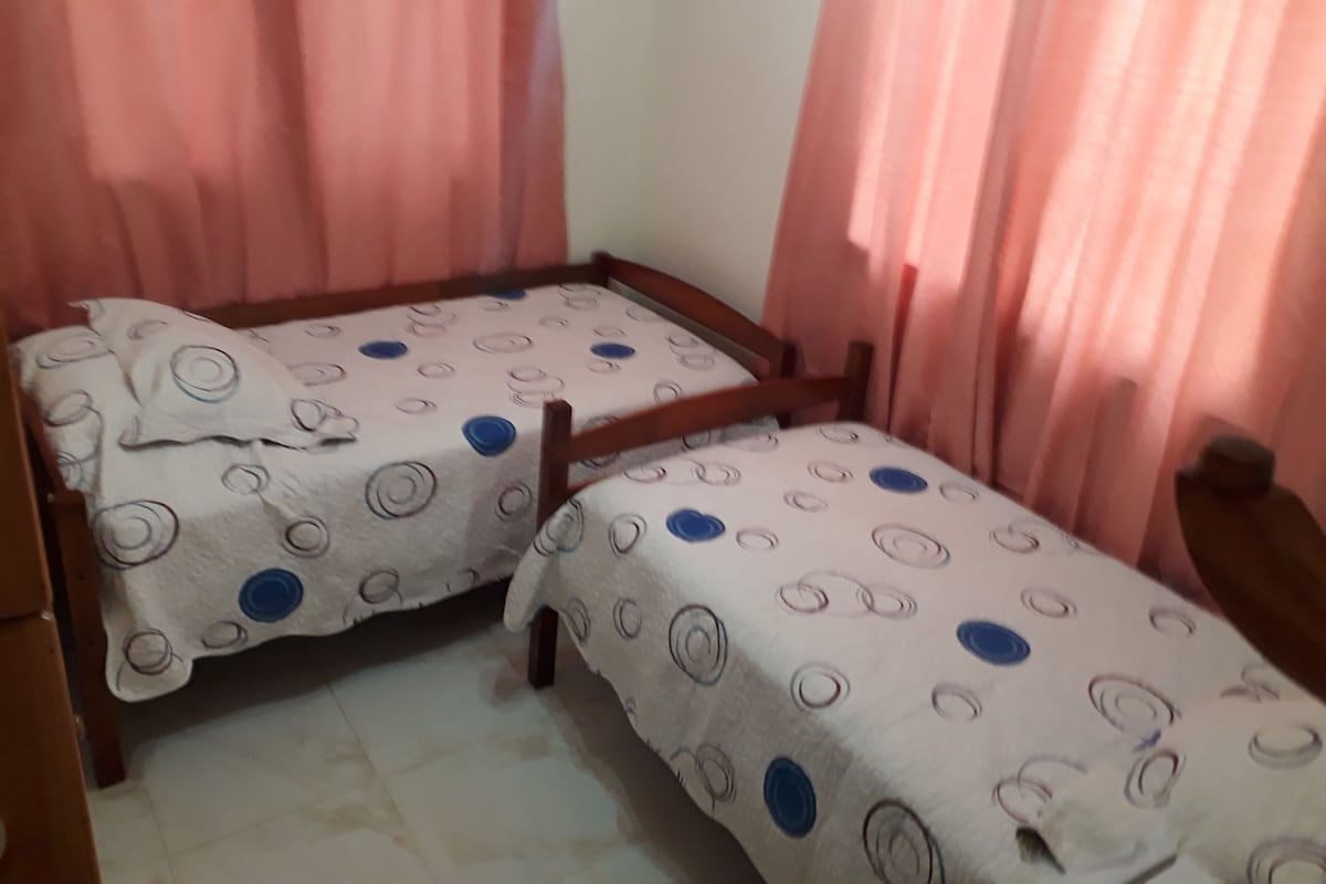 Two single beds with wooden frames and patterned bedding in a room with pink curtains.