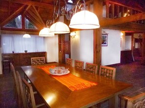 A wooden dining table with chairs, a chandelier, and a window in the background.