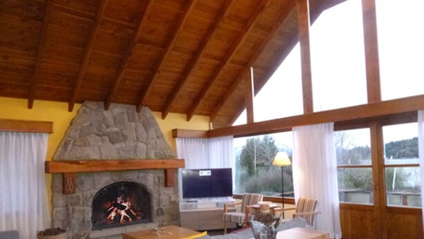 Una sala de estar acogedora con chimenea de piedra, vigas de madera en el techo, asientos cómodos y ventanas amplias.