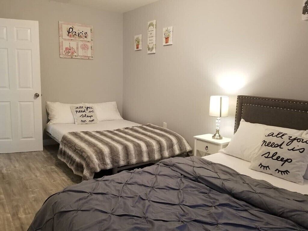 A bedroom with two beds, a nightstand with a lamp, and wall decorations including a 'Paris' sign and a 'Sleep' pillow.
