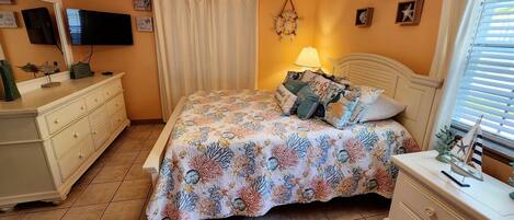 A bedroom with a bed, a nightstand, a dresser, a ceiling fan, a TV, and a window with curtains.