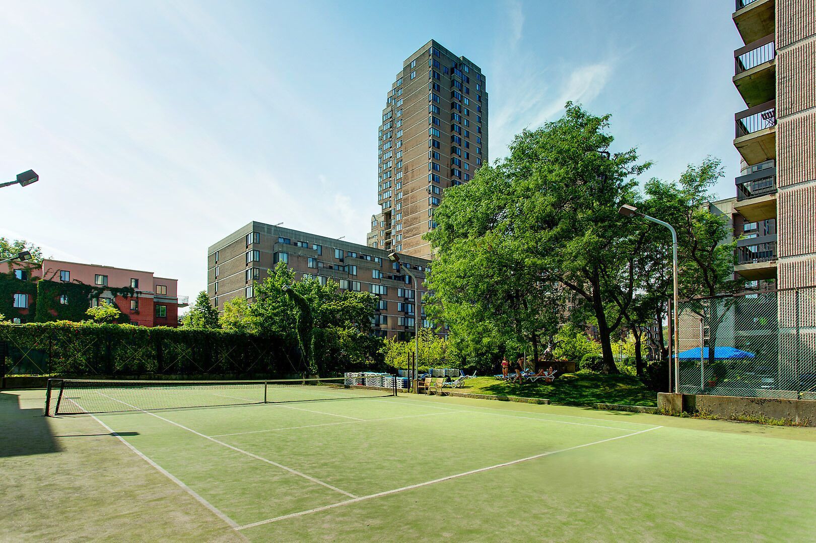 Un court de tennis en plein air, entouré d’arbres et d’immeubles.
