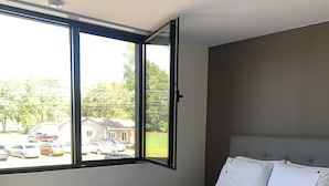 A bedroom with a large window, a bed with white bedding, and a grey headboard.