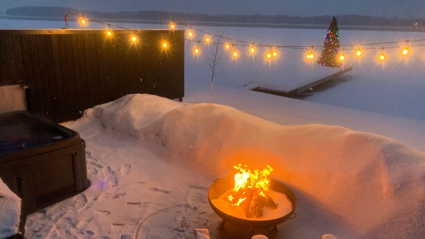 A snow-covered outdoor area with a fire pit, string lights, and a Christmas tree.