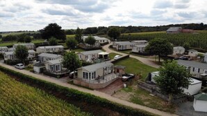 A mobile home park with several single-story homes, a central paved area, and a surrounding grassy field.