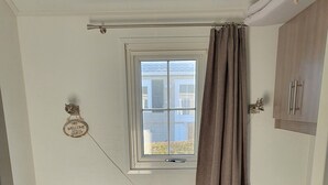 A compact room with two beds, a window with curtains, a welcome sign, and a small cabinet.