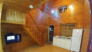 A wooden cabin interior with a kitchen area, a staircase, and a television mounted on the wall. - Yangsan Park Pension (Yangsan)