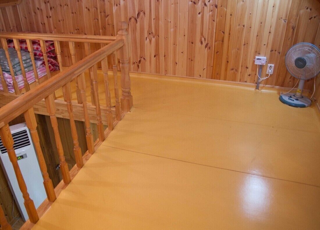 Un escalier en bois menant à un niveau inférieur, un ventilateur sur pied et un appareil de climatisation blanc.
