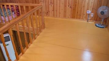 Un escalier en bois menant à un niveau inférieur, un ventilateur sur pied et un appareil de climatisation blanc.