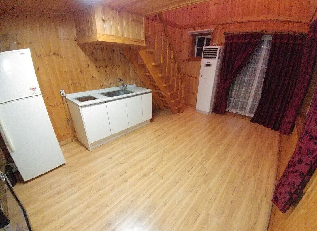 A compact kitchen with wooden walls, a white refrigerator, a sink, and a small window with curtains.