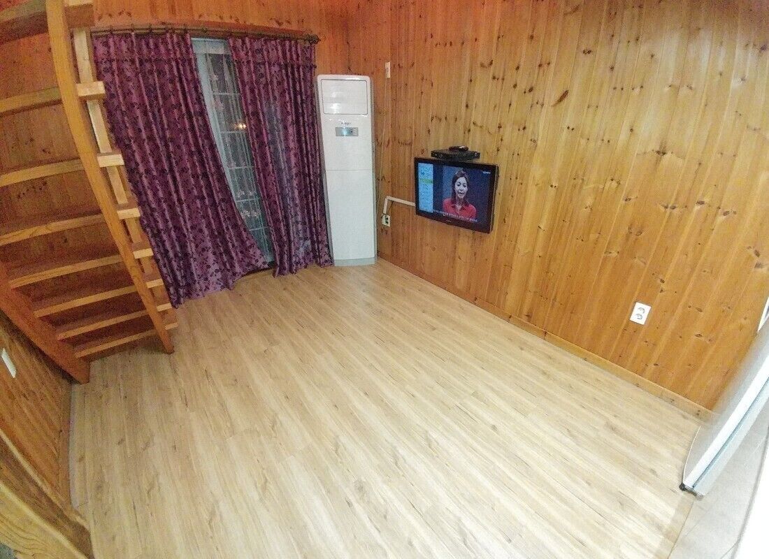 A room with a wooden floor, a white cabinet, a television mounted on the wall, and a wooden staircase.