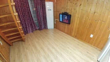 A room with a wooden floor, a white cabinet, a television mounted on the wall, and a wooden staircase.
