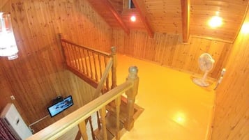 A wooden interior with a staircase, a fan, and a television on the wall.