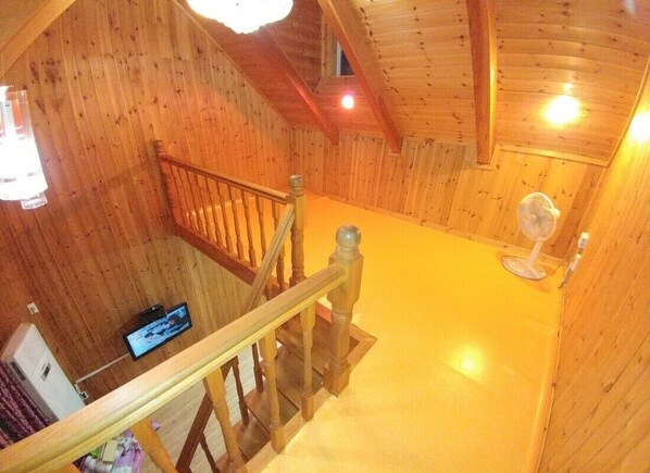 Un interior de madera con una escalera, un ventilador y un televisor en la pared.