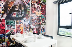 Une pièce dont un mur est recouvert de posters de bandes dessinées, ornée d’une grande flèche décorative, et comprenant une table avec de la vaisselle blanche.