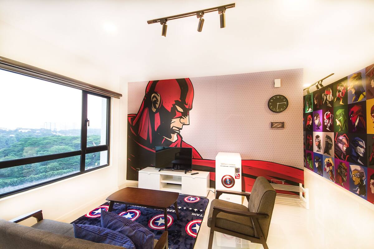 A room with a large window, a desk, a chair, a TV, a heater, and a wall with superhero posters.