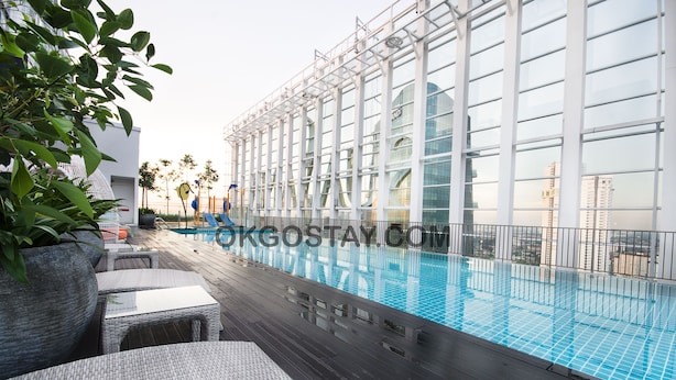 A rooftop pool area with a glass railing, lounge chairs, and potted plants. - Zenith Suites JBCC by OKGOSTAY (Johor Bahru)