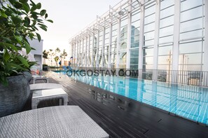 Un espace piscine aménagé sur le toit, doté d’une rambarde en verre, de chaises longues et de plantes en pot.