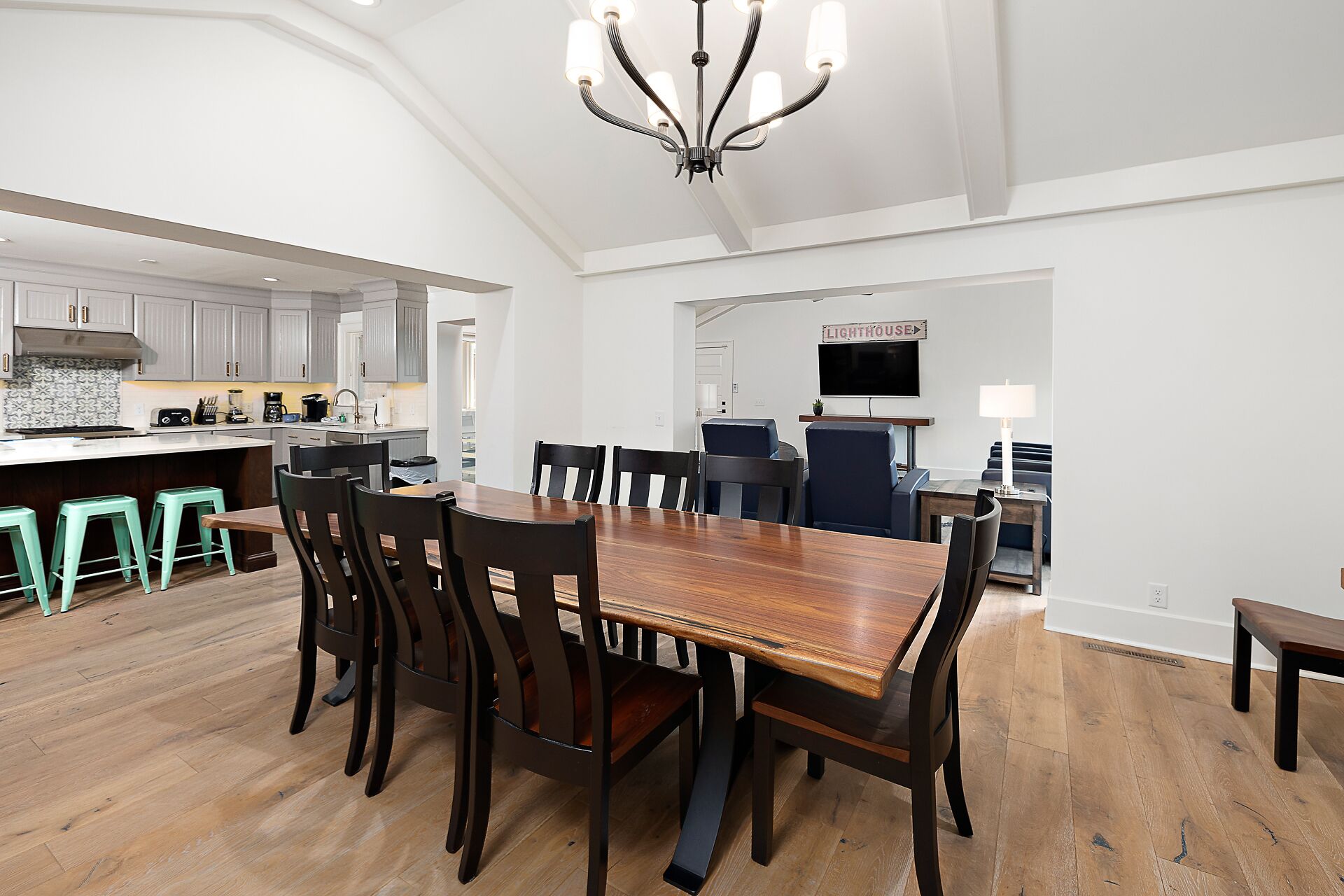 A spacious dining area with a large wooden table and dark chairs, a kitchen with white cabinets, and a chandelier.