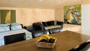 A room with a wooden ceiling, a dining table with a fruit basket, a sofa, and two paintings on the walls.