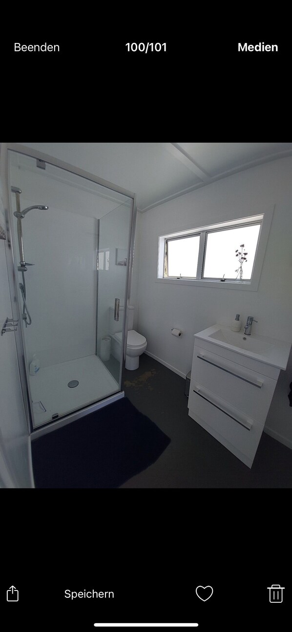 A modern bathroom with a glass-enclosed shower, a white sink, and a small window. - Rural property with views of Rangataua Bay (Tauranga)