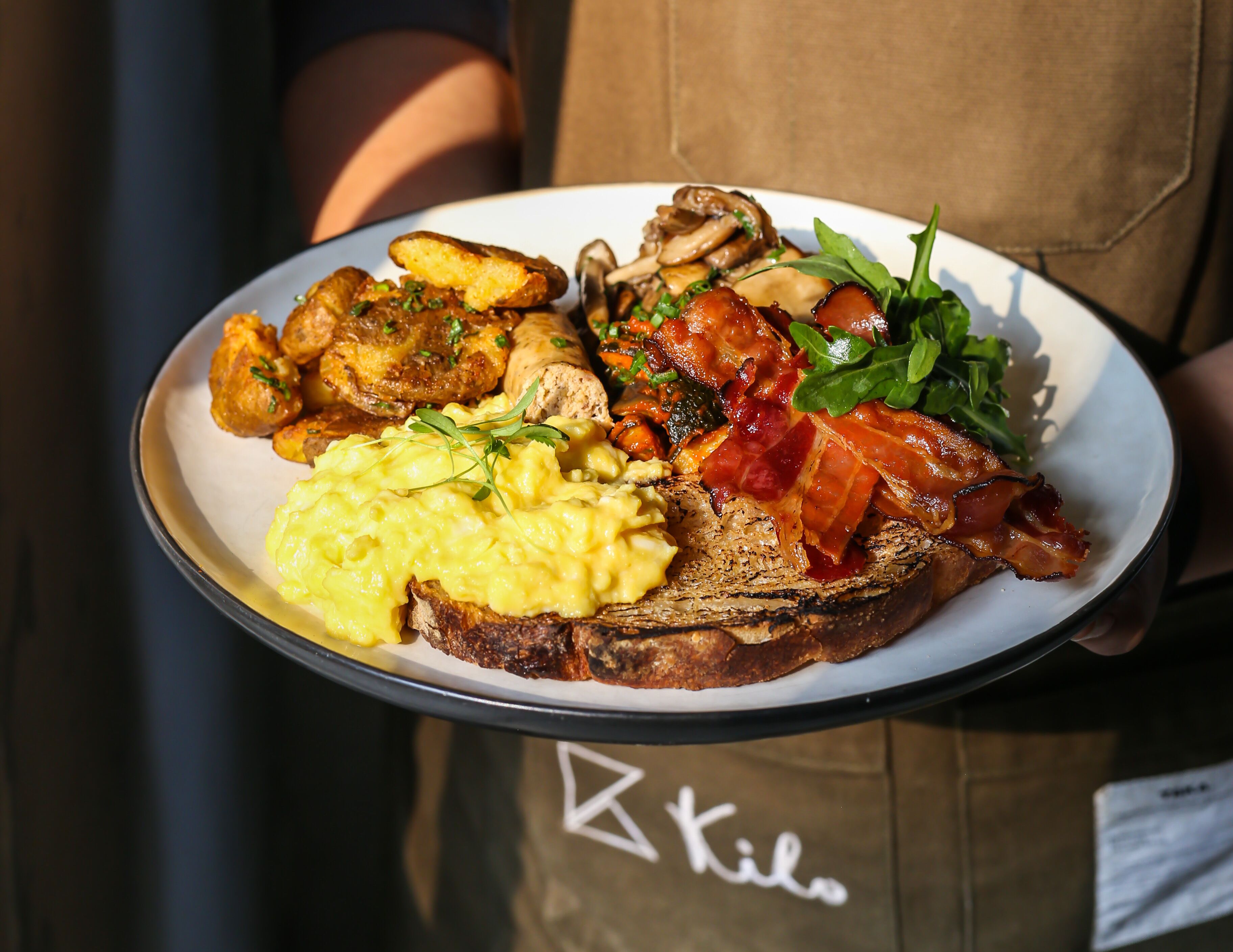 A plate of food including scrambled eggs, bacon, mushrooms, and toast.